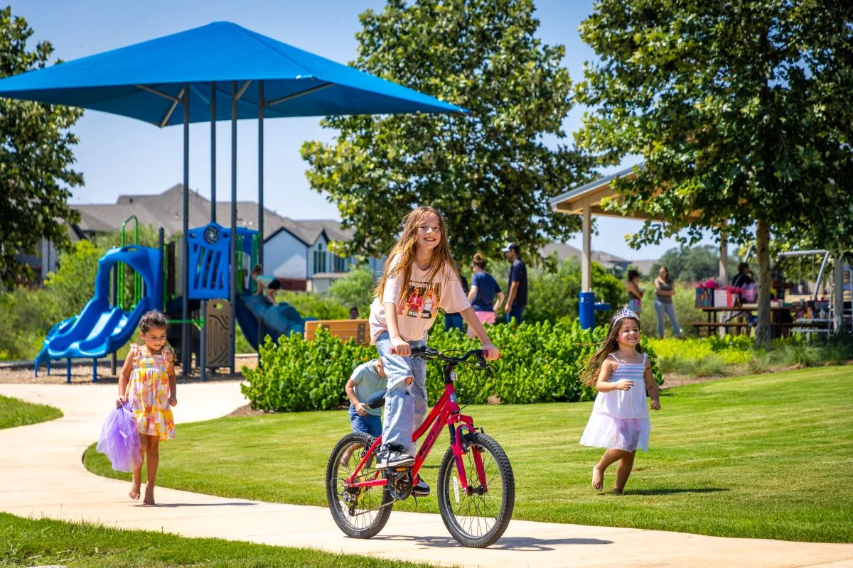 A young girl riding a bicycle with kids in the background in Veramendi. 